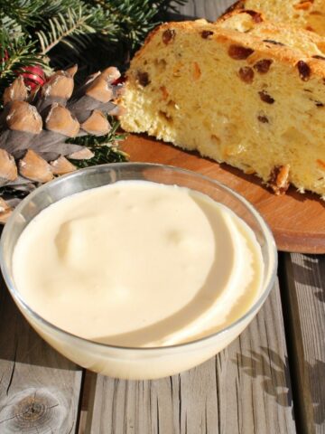 A close up of Italian Mascarpone Custard in a bowl. On the side there are some Panettone slices and pine branches and cones