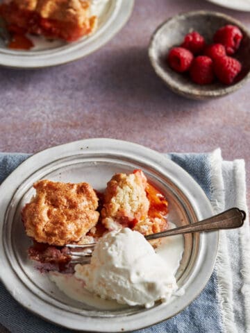 Slice of Peaches and Raspberries Cobbler in a white plate. The slice shown all fruit baked inside. It is served with some ice-cream