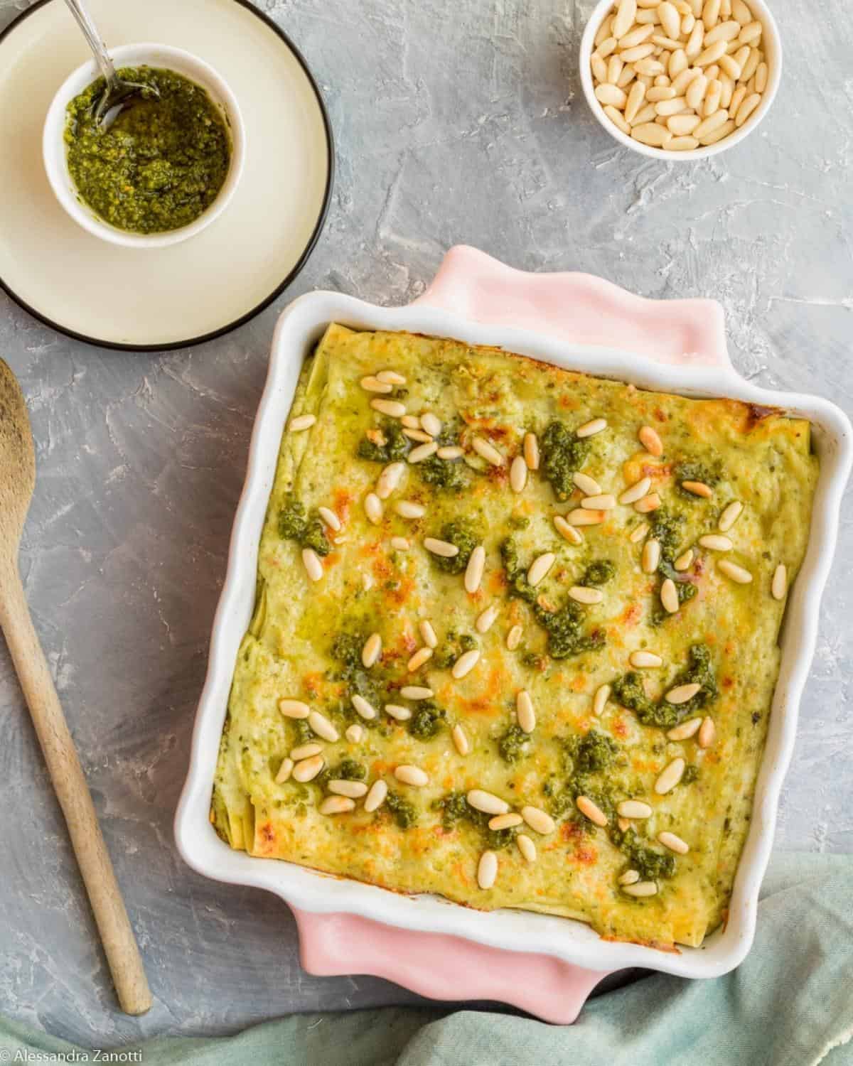 A view from above Pesto Lasagna in a pink pan. It is topped with pesto sauce and pine nuts