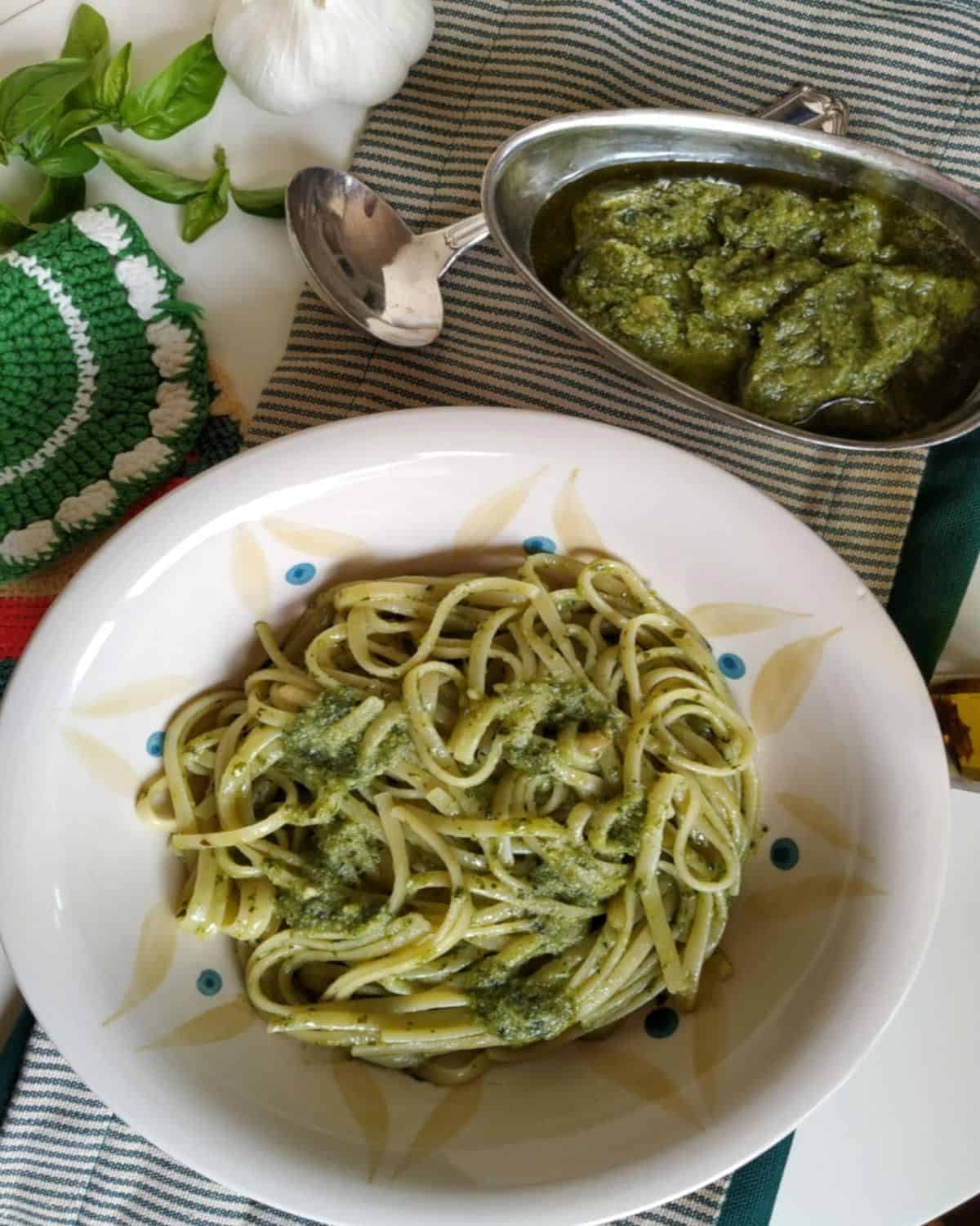 Pesto pasta from above in a white plate. A bowl with pesto on the side