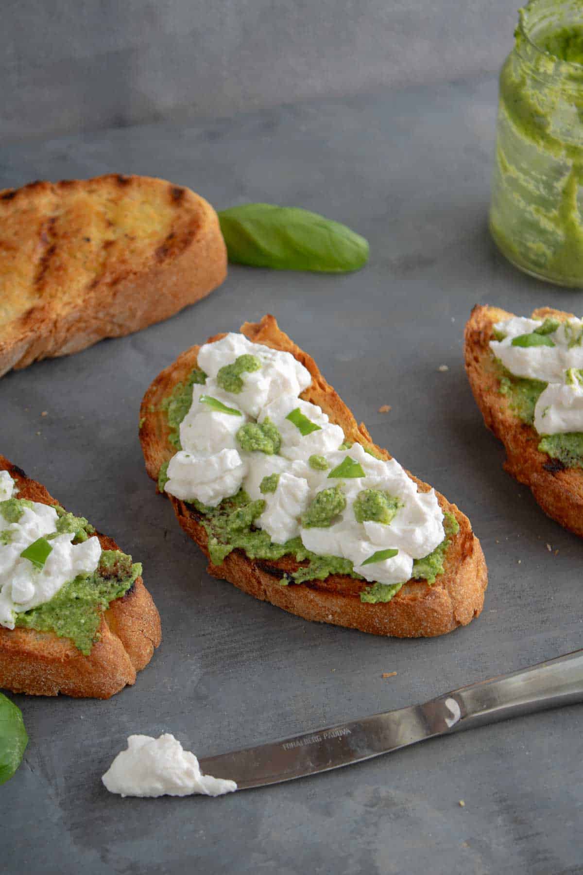 A close up of a few Italian Pesto Bruschetta with Ricotta in a grey table. The bread is spread with cheese and pesto