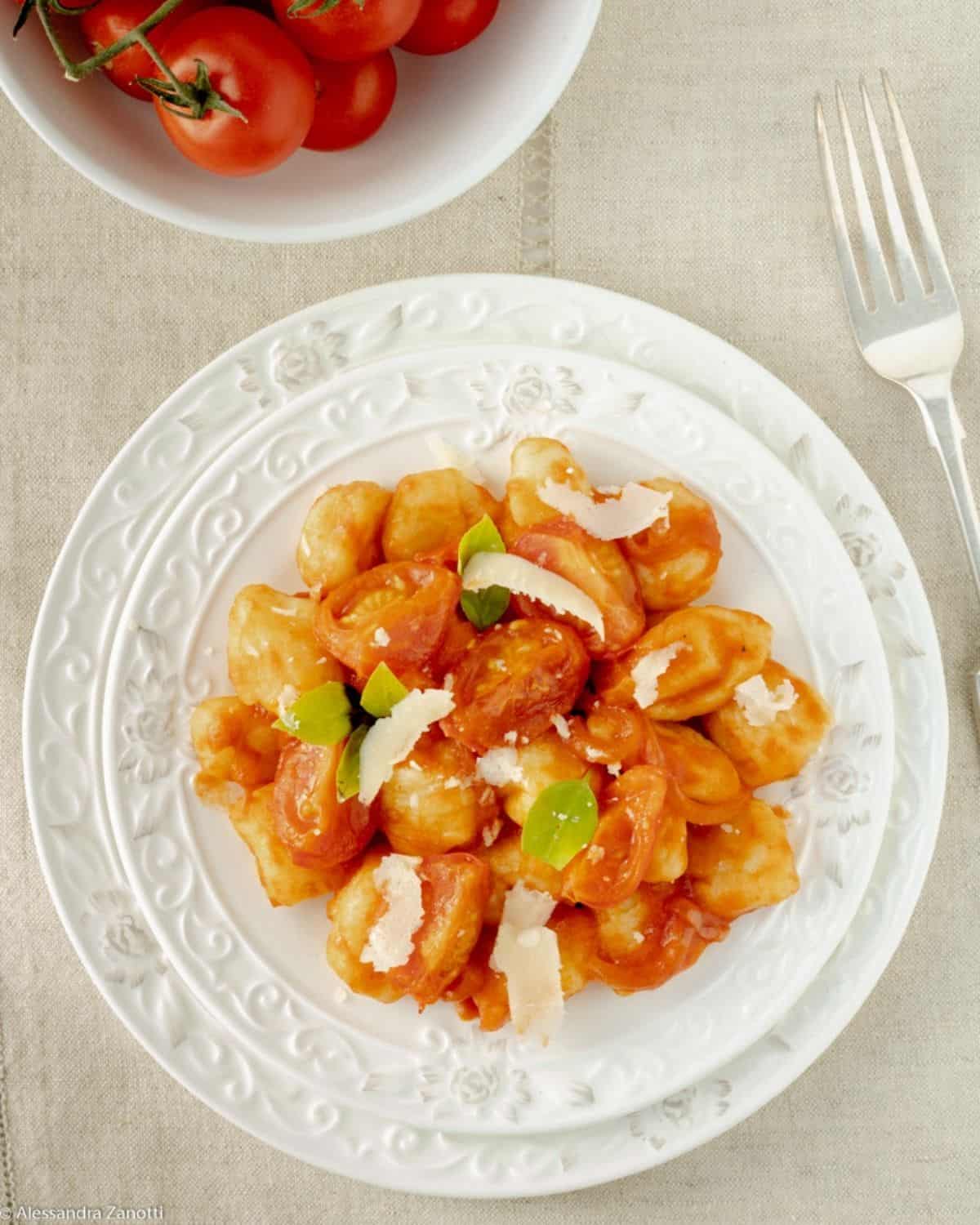Potato Gnocchi in white plate with fork on light linen. Gnocchi are served with tomato sauce, Parmesan cheese and basil leaves