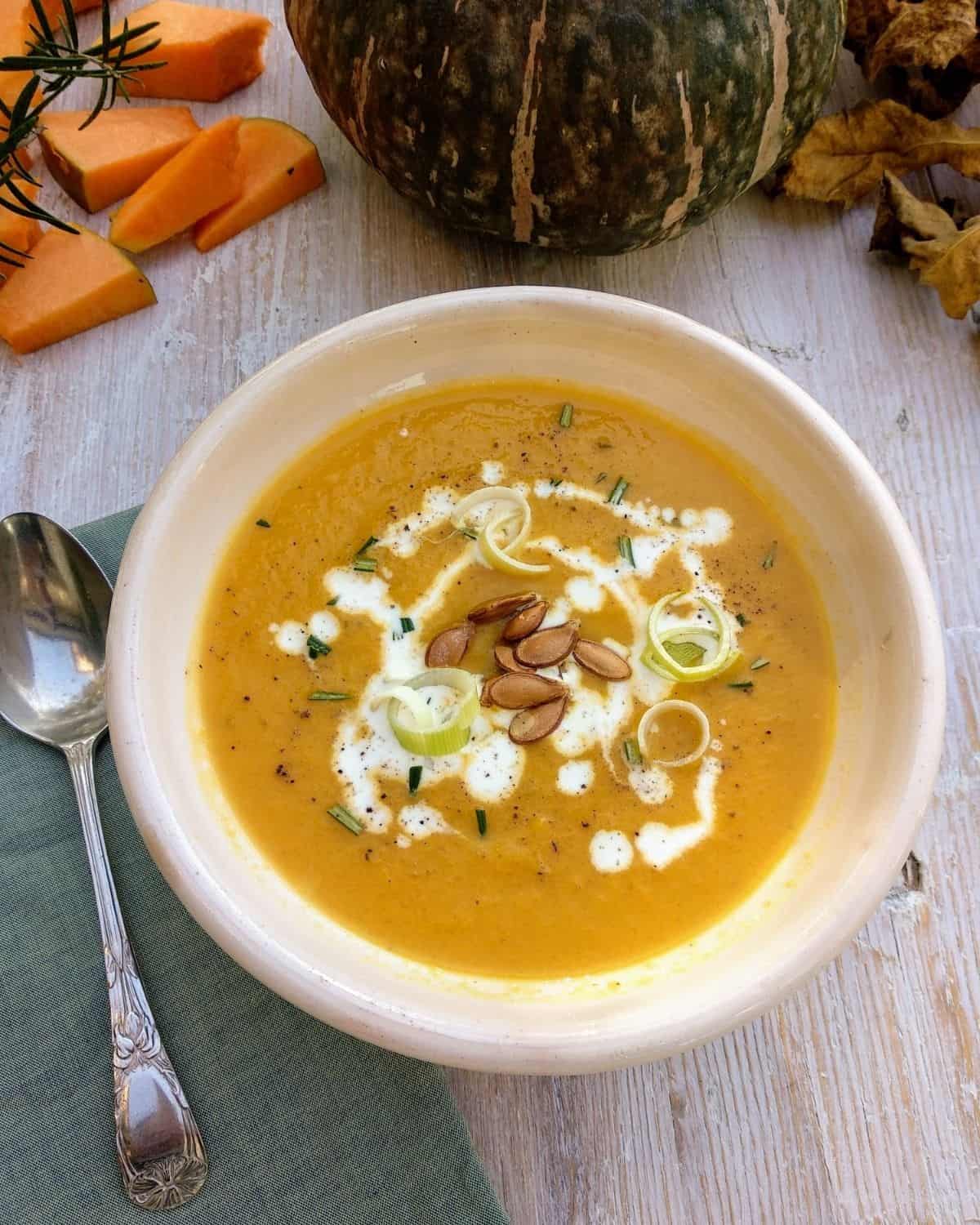 A bowl of pumpkin soup view from above. It’s garnished with seeds and cream