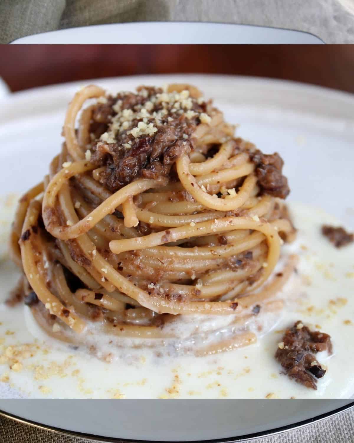 Spaghetti with Italian Radicchio in a white plate. Pasta sit on a cheese layer and it is topped with radicchio and walnut kernels