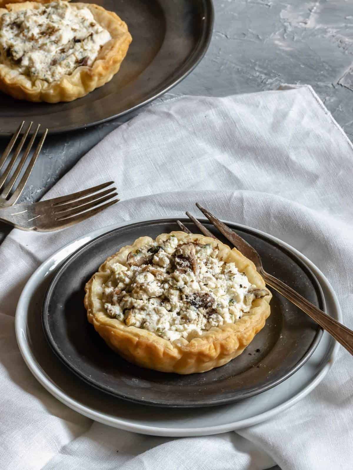 puff-pastry-tart-ricotta-and-mushrooms-truffle-on-plate-with-fork-dish-with-another-tart-in-the-background