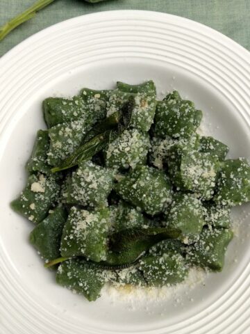 Ricotta and Spinach Gnocchi on a white plate and green linen. Gnocchi are topped with grated Parmisan cheese