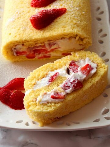 a close up photo of Strawberry And Ricotta Roll on a white plate showing the whipped cream and strawberries inside the cake