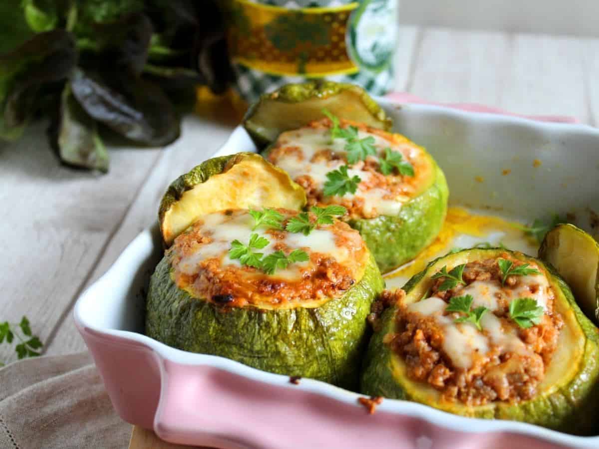 Stuffed Round Zucchini in a pink pan on a light wooden table. Zucchini are filled with meat and cheese