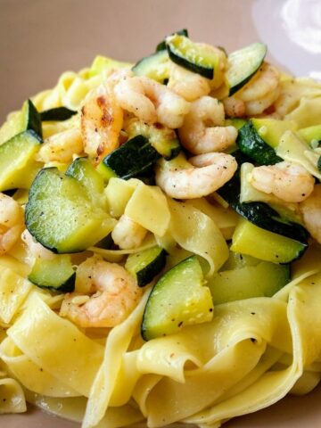 A close up of an Italian Tagliatelle with Praws and Zucchini in a light pink plate.