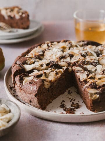 Two slices of Chocolate and Pear Cake on a grey rustic table. The slices shown the pears baked inside and almonds on top