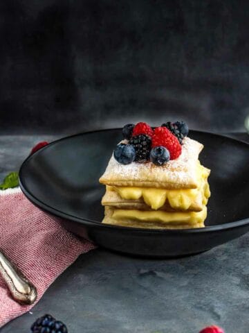 A slice of Millefoglie with Vanilla Custard and Wild Berries-on-a-black-dish-showing-the-custard-inside