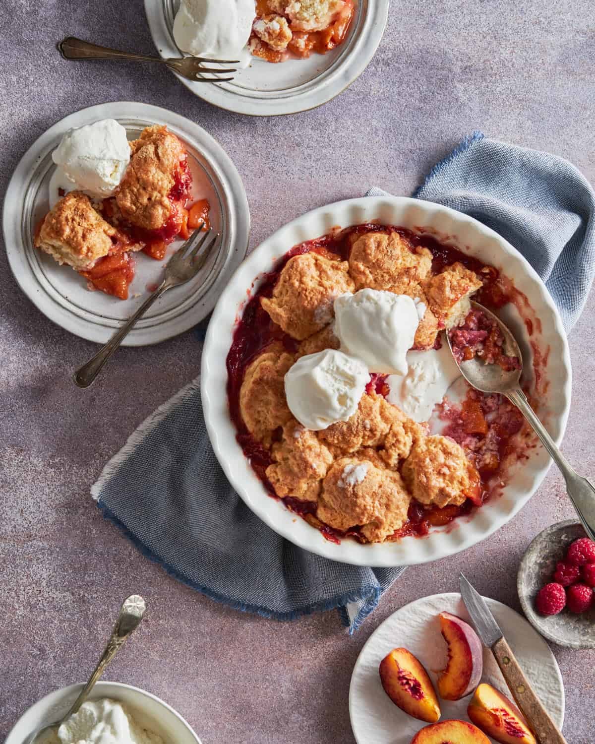 Peaches and Raspberries Cobbler in the baking tray and slices in plates served with ice-cream. Peaches and Raspberries aside.